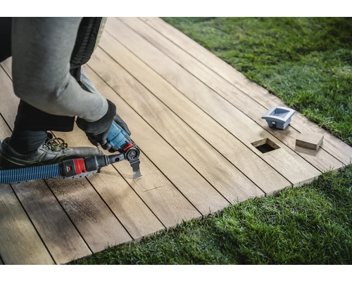 Handwerker bearbeitet eine Holzterrasse mit einem Multifunktionswerkzeug