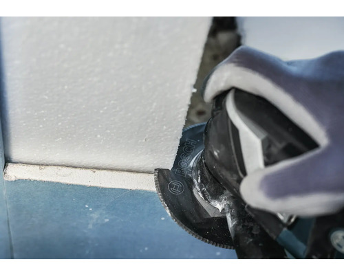Handwerker bei der Arbeit mit einer oszillierenden Säge zum Schneiden von Materialien in einer Baustelle. Bosch Logo.