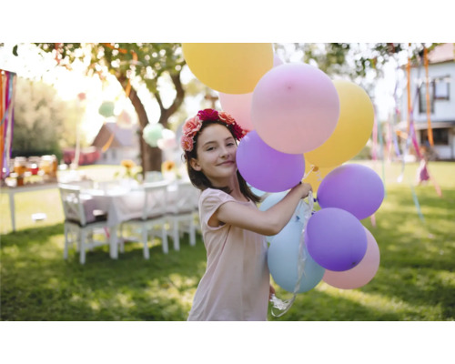 Mädchen mit Blumenkranz und Luftballons im Garten für eine Gartenparty