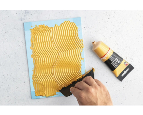 Auftragen von Strukturpaste auf eine Leinwand mit einer Spachtel neben einer Tube Strukturpaste.