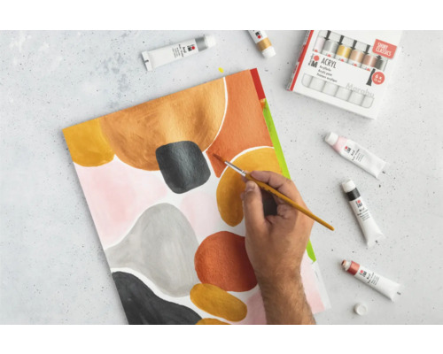 Person malt mit Acrylfarben ein abstraktes Gemälde. Farbtuben und Pinsel liegen bereit.