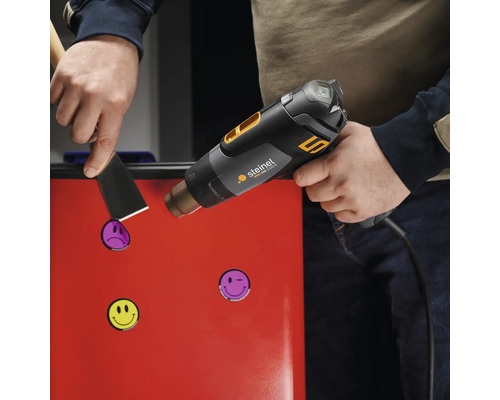 Person entfernt Aufkleber mit Heißluftpistole von einer roten Oberfläche