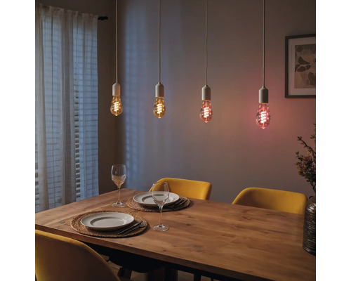 Esstisch mit vier hängenden Glühbirnen, die unterschiedliche Lichtfarben ausstrahlen.