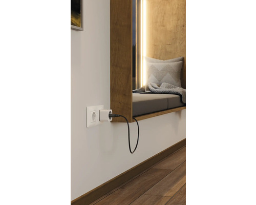 Steckdose mit Stecker in einem hellen Raum mit Fensterbank und Sitzgelegenheit.