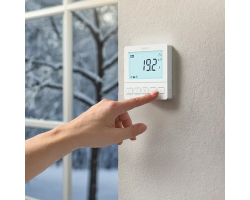 Eine Hand bedient ein Hama Thermostat an der Wand.