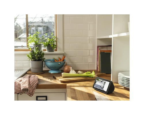 Küchenszene mit Gemüseschale, Kräutertöpfen und einem digitalen Gerät auf einer Arbeitsfläche