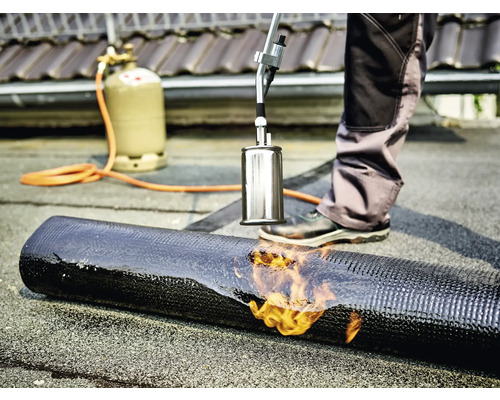 Dachdecker schweißt Bitumenbahn mit einem Brenner und einer Gasflasche.