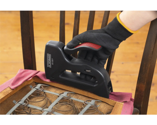 Eine Hand mit Handschuh verwendet einen Tacker, um einen Stuhl neu zu beziehen.