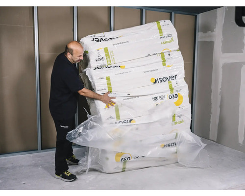 Ein Mann stapelt Pakete mit Isover Dämmwolle in einem Raum.