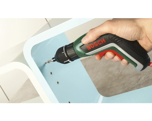 Eine Hand schraubt mit einem Akkuschrauber von Bosch eine Schraube in ein hellblaues Möbelstück