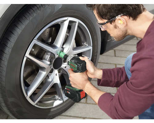 Mann wechselt mit einem Akku-Schlagschrauber einen Reifen an einem Auto