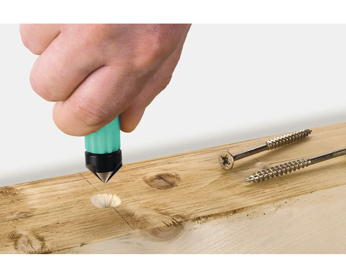 Eine Hand verwendet einen Körner auf einem Holzbrett neben zwei Schrauben.