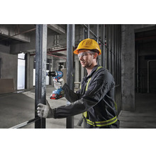 Ein Arbeiter mit Schutzhelm und Schutzbrille benutzt einen Akku-Bohrschrauber auf einer Baustelle.