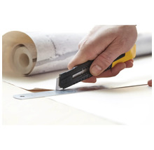 Eine Hand schneidet mit einem Cuttermesser und einem Lineal Tapete zu.