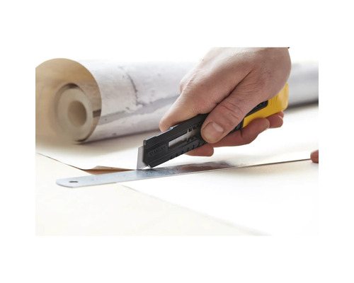 Eine Hand schneidet mit einem Cuttermesser und einem Lineal Tapete zu.