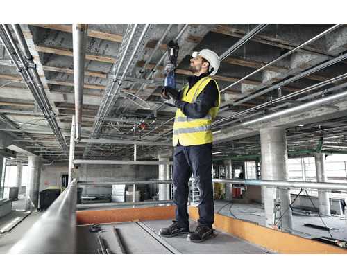 Ein Arbeiter montiert Rohre an der Decke eines Rohbaus mit einer Rohrzange.