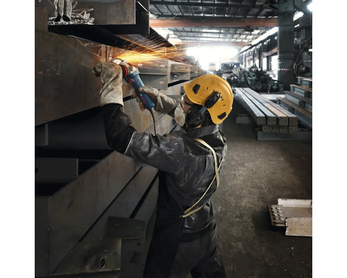 Ein Arbeiter schleift Metall mit einem Winkelschleifer in einer Werkshalle, während Funken sprühen.