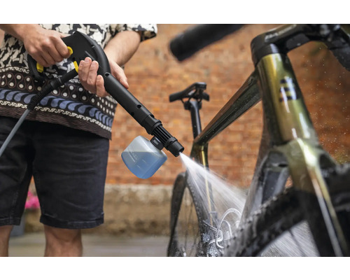 Eine Person reinigt ein Fahrrad mit einem Hochdruckreiniger und einer Schaumdüse.