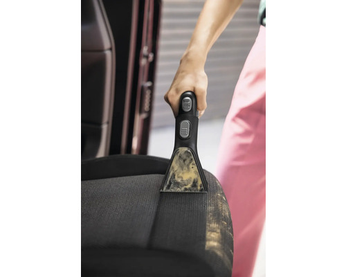 Detailaufnahme einer Person, die mit einem tragbaren Fleckenreiniger einen Autositz reinigt.