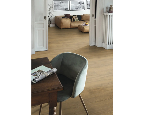 Innenaufnahme eines Raumes mit Holzboden, einem Tisch, einem Stuhl und einem Wohnbereich im Hintergrund.