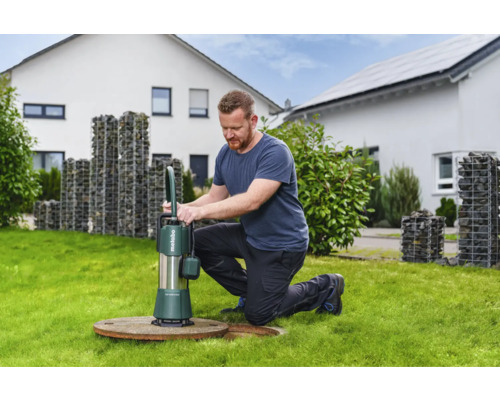 Mann bedient eine Metabo Tauchpumpe auf einer Rasenfläche vor einem Haus. Die Pumpe dient zur Wasserentfernung.