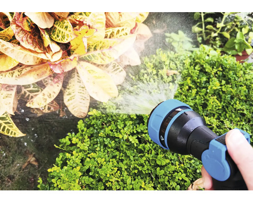 Eine Hand hält einen Gartenschlauch, der Pflanzen bewässert.