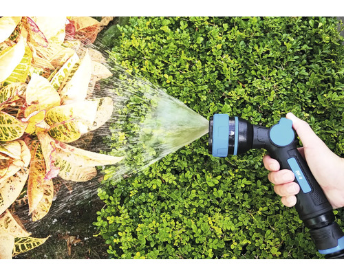 Eine Hand hält eine Gartenspritze, die Wasser auf Pflanzen sprüht.