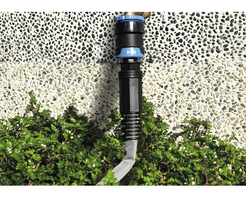 Gartenschlauch-Verbindungsstück vor einer Wand und Büschen