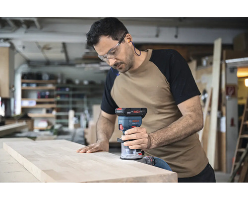 Ein Mann benutzt eine Oberfräse auf einem Holzbrett in einer Werkstatt.