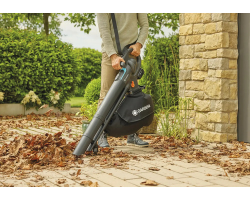 Eine Person benutzt einen Akku-Laubsauger von Gardena im Garten, um Laub aufzusammeln.