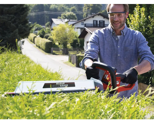 Mann schneidet Hecke mit einer elektrischen Heckenschere im Garten.