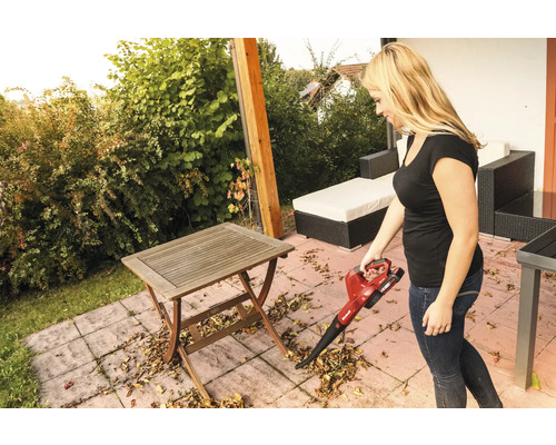 Frau benutzt einen Akku-Laubsauger auf einer Terrasse mit Tisch und Gartenmöbeln.