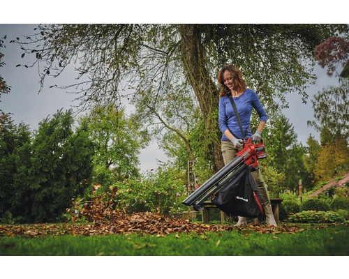 Eine Frau benutzt einen Laubsauger im Garten, um Laub zu entfernen.