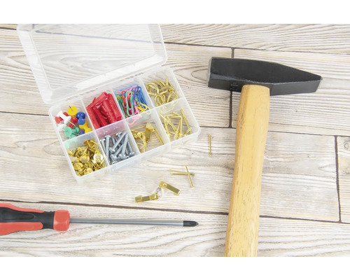 Hammer, Schraubendreher und Sortimentskasten mit Schrauben, Dübeln, Nägeln, Reißzwecken und Büroklammern auf einer Holzoberfläche