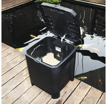 Automatische Fischfuttermaschine mit geöffnetem Deckel neben einem Teich
