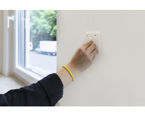 Eine Person bedient einen Lichtschalter an einer Wand neben einem Fenster.