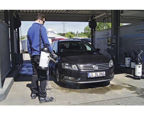 Ein Mann reinigt ein Auto mit einem Drucksprüher in einer Autowaschanlage.