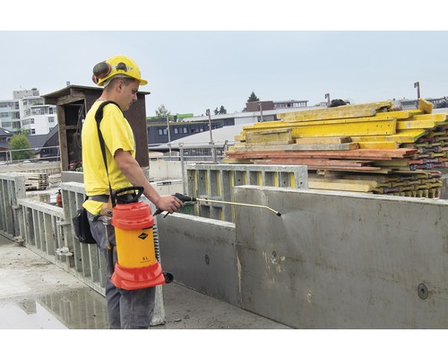 Ein Bauarbeiter verwendet ein Sprühgerät zur Behandlung von Betonformen auf einer Baustelle.