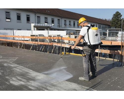 Bauarbeiter verwendet eine Rückenspritze auf einer Betonoberfläche.