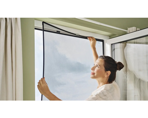 Frau montiert Insektenschutzgitter am Fenster