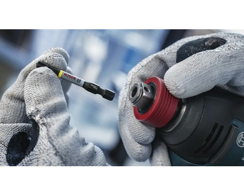 Eine Hand mit Handschuh hält einen Bosch Schrauberbit bereit, um ihn in einen Akkuschrauber einzusetzen.