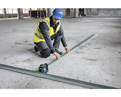 Ein Bauarbeiter nivelliert mit einem Linienlaser einen Boden.