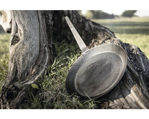 Metall Bratpfanne mit Griff liegt auf einem Baumstumpf im Freien.