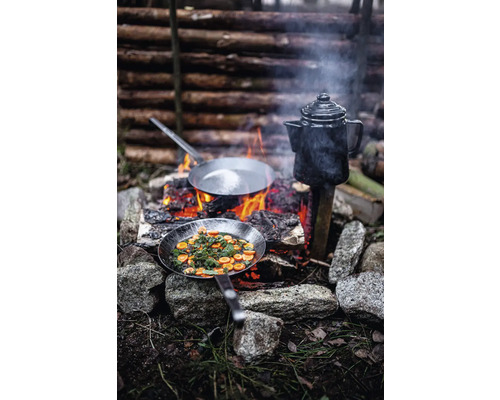 Zubereitung von Speisen im Freien mit zwei Bratpfannen und einer Kaffeekanne über einem offenen Feuer.