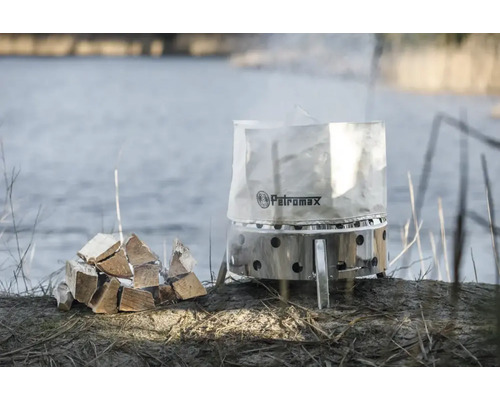 Petromax Feuertopf mit Holzstapel am Seeufer