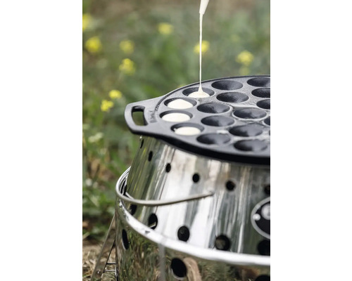 Poffertjes-Pfanne aus Gusseisen auf einem Grill, während Teig in die Mulden gegossen wird