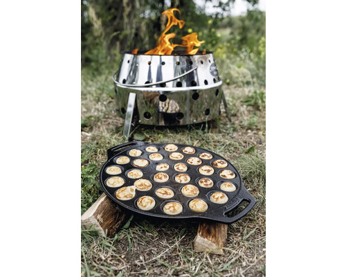 Poffertjespfanne auf Holzscheiten mit Feuerkorb im Hintergrund