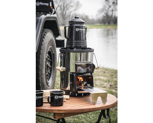 Petromax Holzvergaserkocher mit Kaffeekanne und Emaille Tassen auf einem Holztisch im Freien