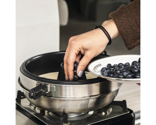 Frau dekoriert Kuchen mit Blaubeeren in einer runden Kuchenform auf einem Gasherd