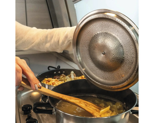 Nudeln werden in einem Topf mit einem Holzlöffel umgerührt, während der Deckel des Topfes angehoben wird.